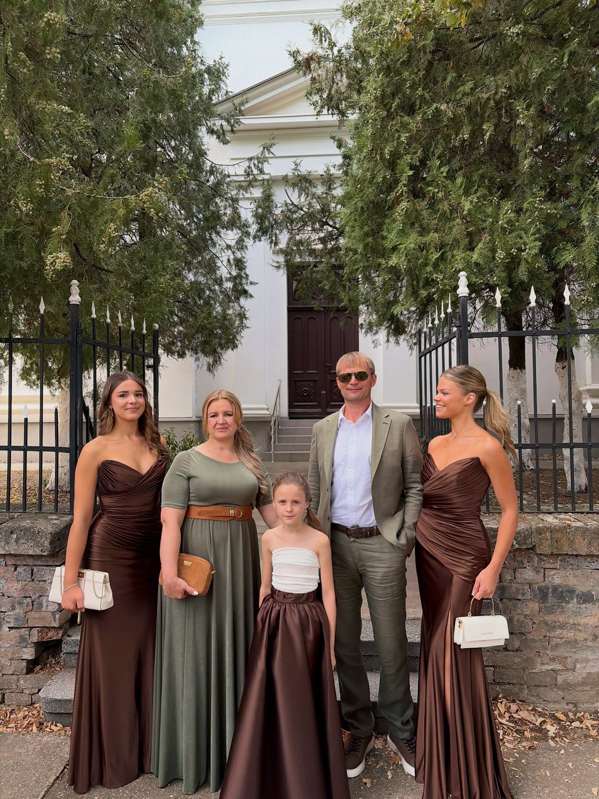 A family of five posing in coordinated earthy-toned formal outfits in front of a white building.