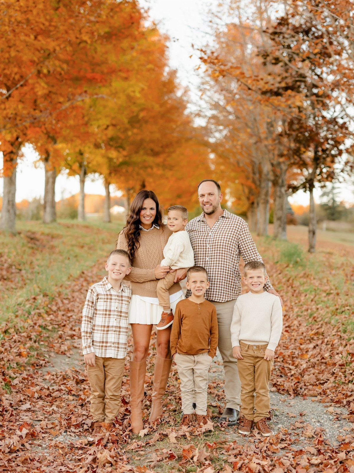 A family of five posing together in a field of autumn leaves and orange trees.