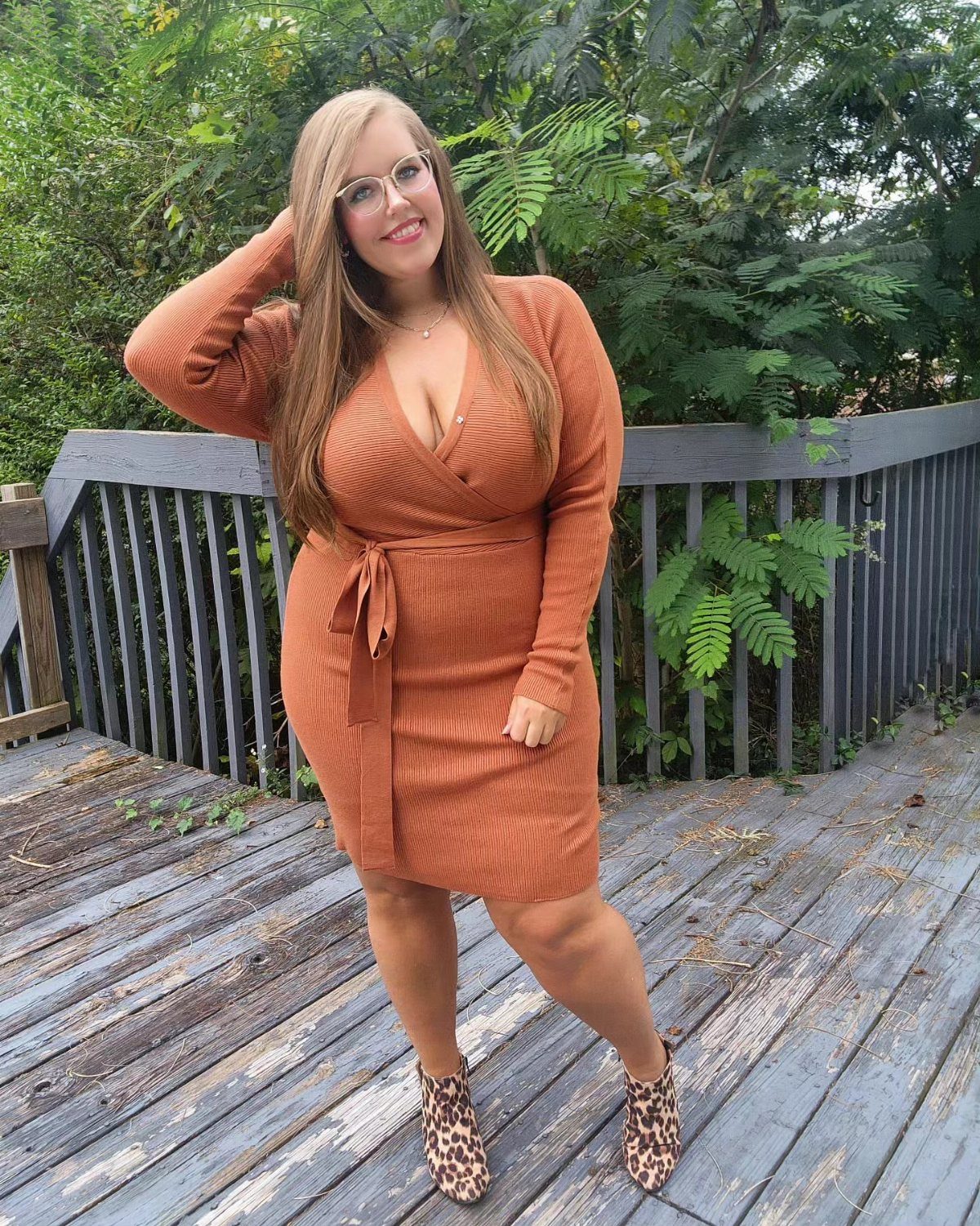 A smiling woman in an orange knit wrap dress and leopard print boots posing outdoors.