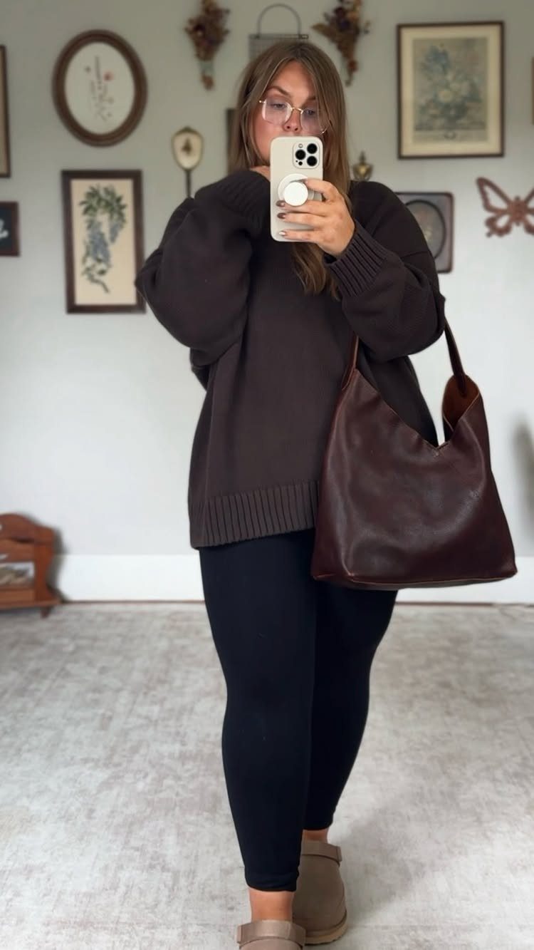 A woman in a brown sweater and black leggings posing for a mirror selfie.