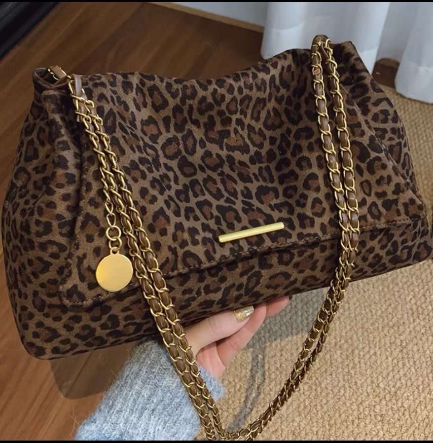 A leopard-print fabric handbag with a gold chain strap held by a person's hand.