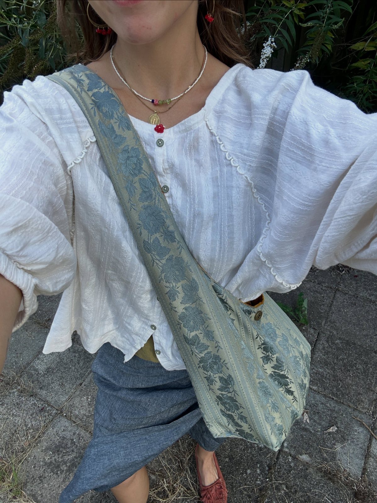 Person wearing a white blouse and carrying a blue patterned tapestry crossbody bag.