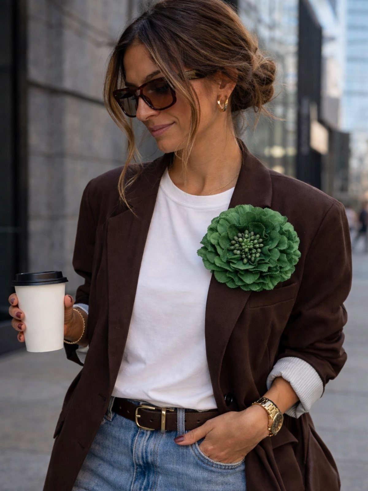 Woman wearing a brown blazer with a large green floral brooch pinned to the lapel.
