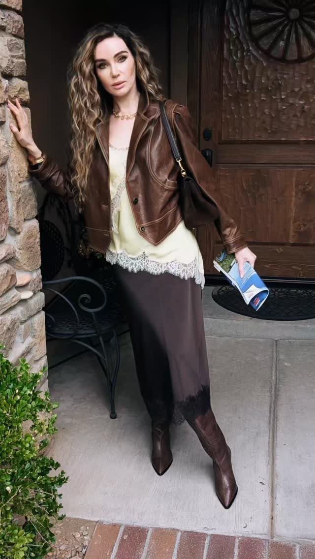 Woman wearing a brown leather jacket, cream lace top, and dark brown lace midi skirt.