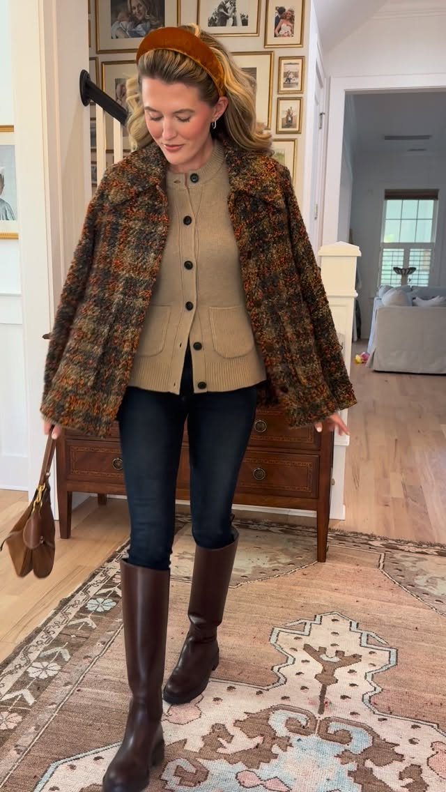 A woman wearing a tan cardigan, dark jeans, and tall brown leather riding boots.
