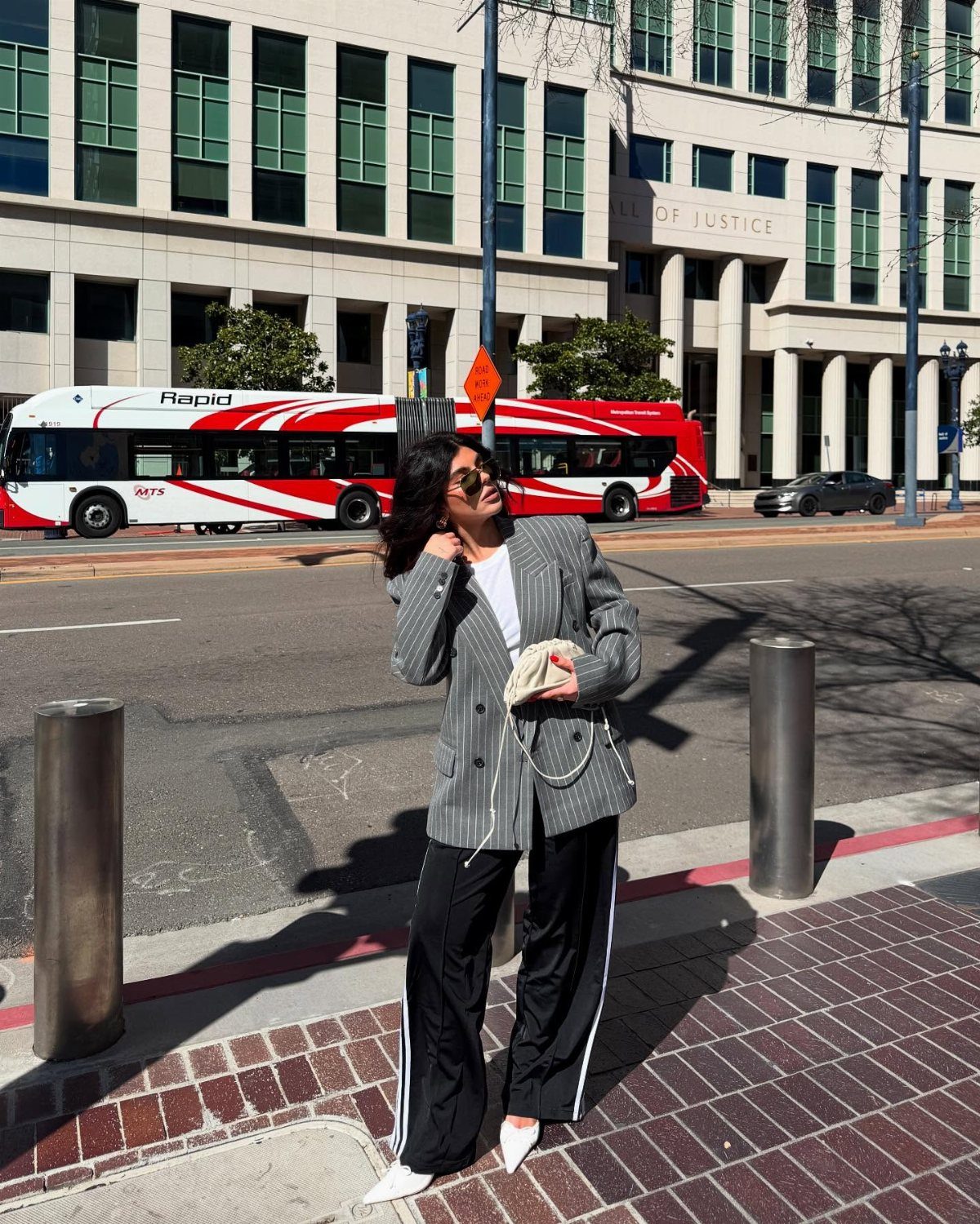 A woman posing in a pinstripe blazer and black track pants with white stripes on a city street.