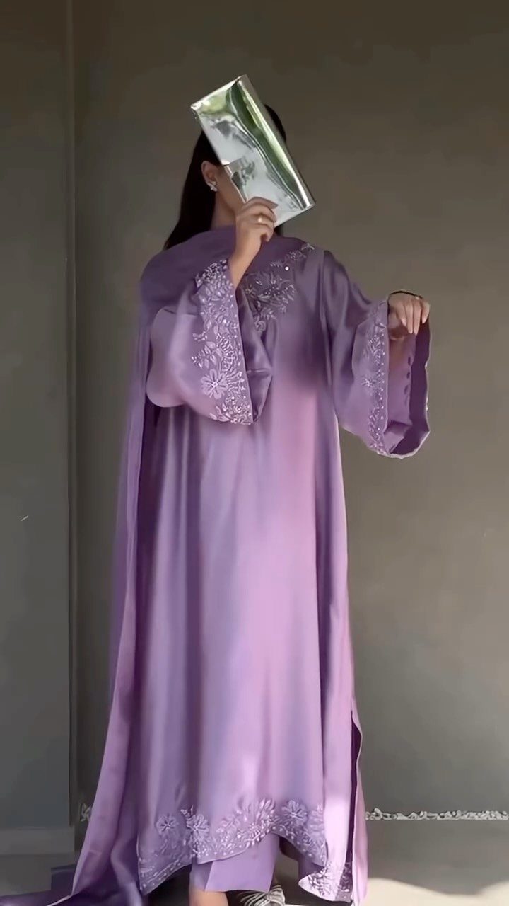 A person in a long lavender silk gown with silver embroidery holding a silver clutch.