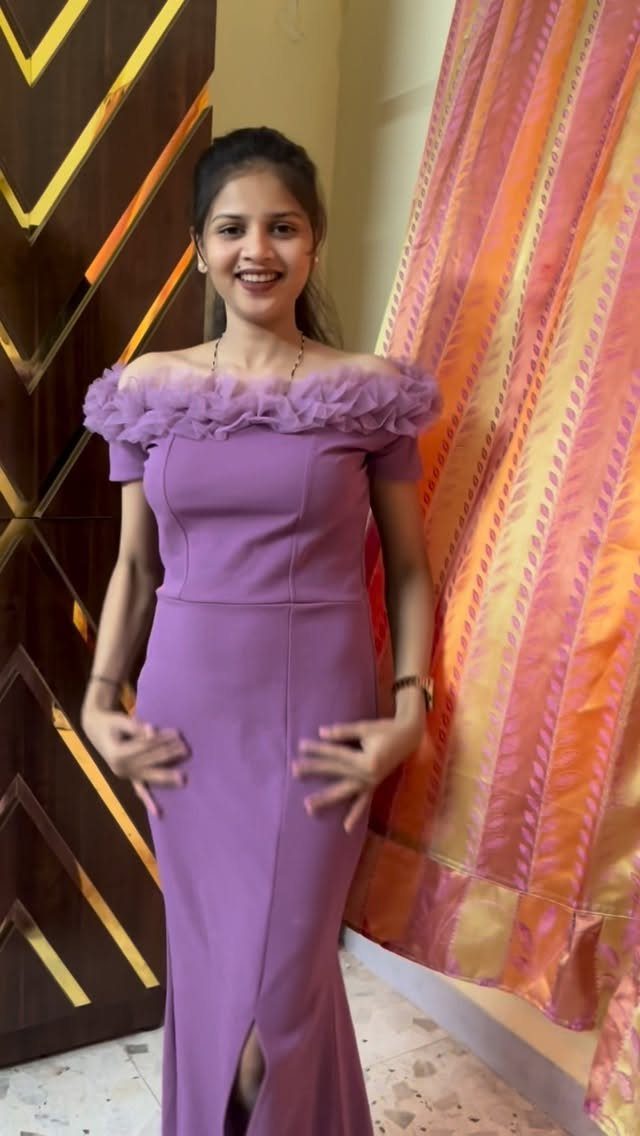 A smiling woman wearing a long purple off-the-shoulder mermaid dress with ruffled tulle.