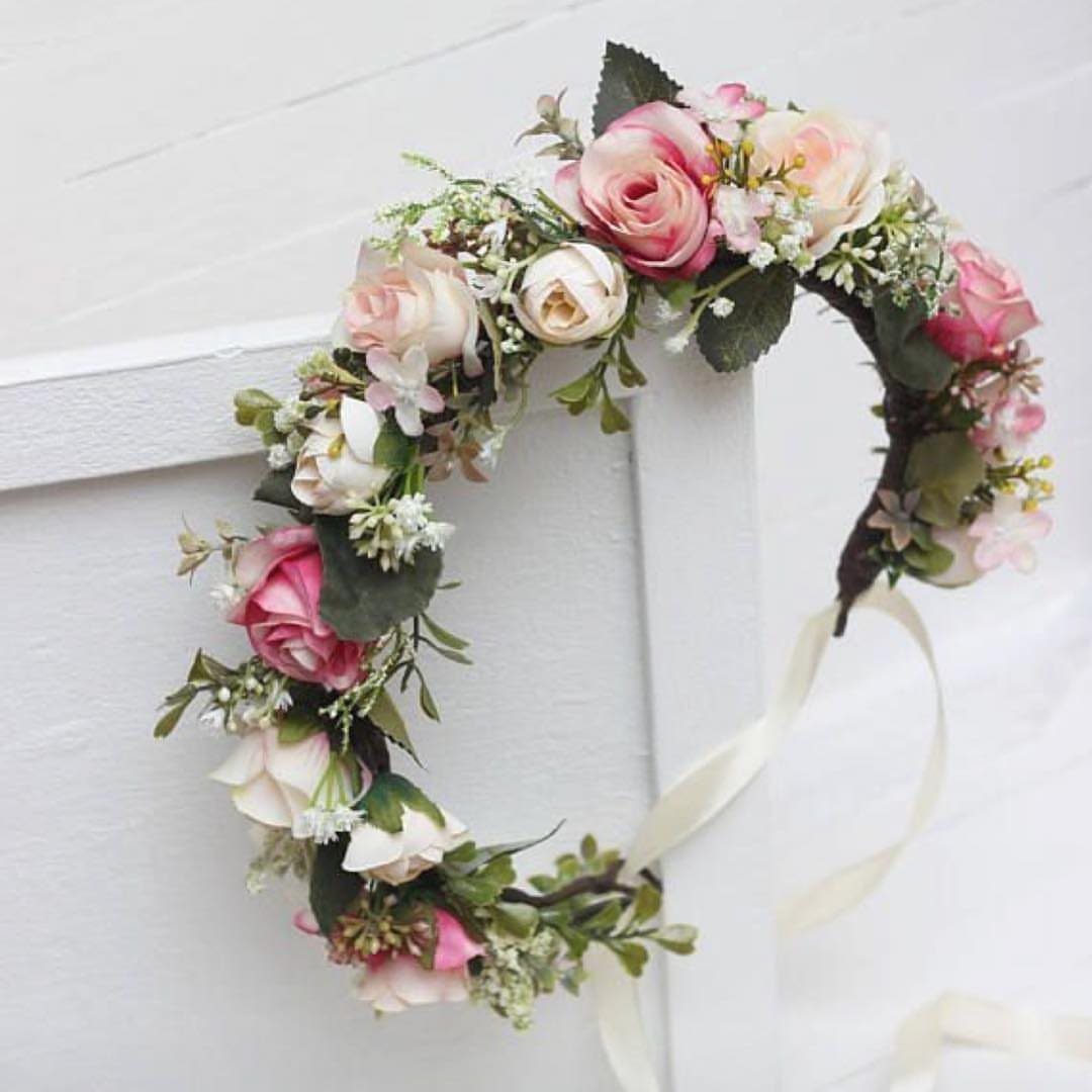 A delicate floral crown featuring pink and white roses with green leaves on a white background.