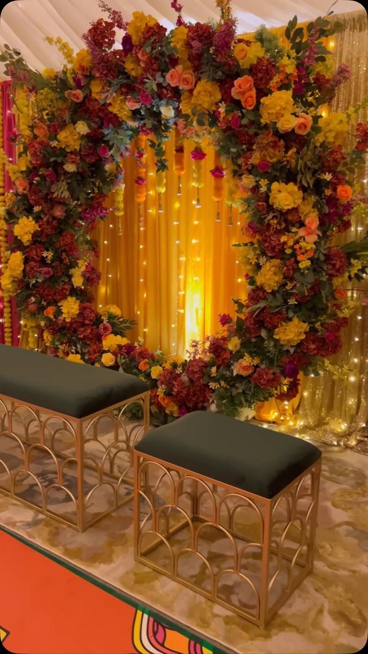A large circular floral wreath with warm lights and gold ottomans in a decorated setting.