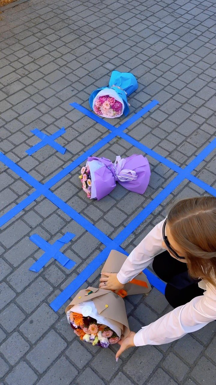 A person placing a flower bouquet on a blue tape tic-tac-toe grid outdoors.