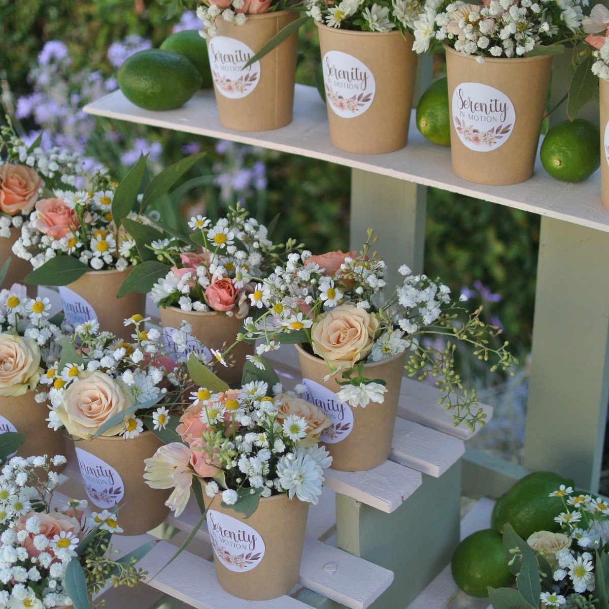 Small paper cups filled with delicate peach and white flowers arranged on wooden shelves.