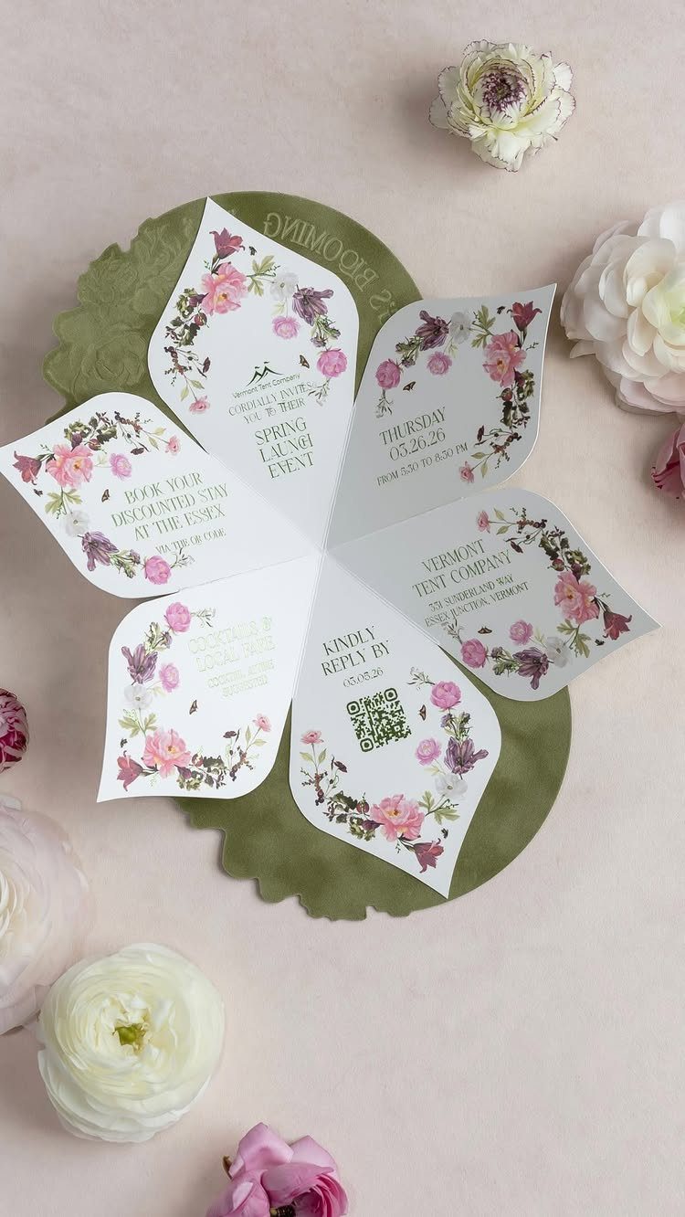 Flower-shaped invitations with floral patterns arranged on a green base surrounded by real blossoms.