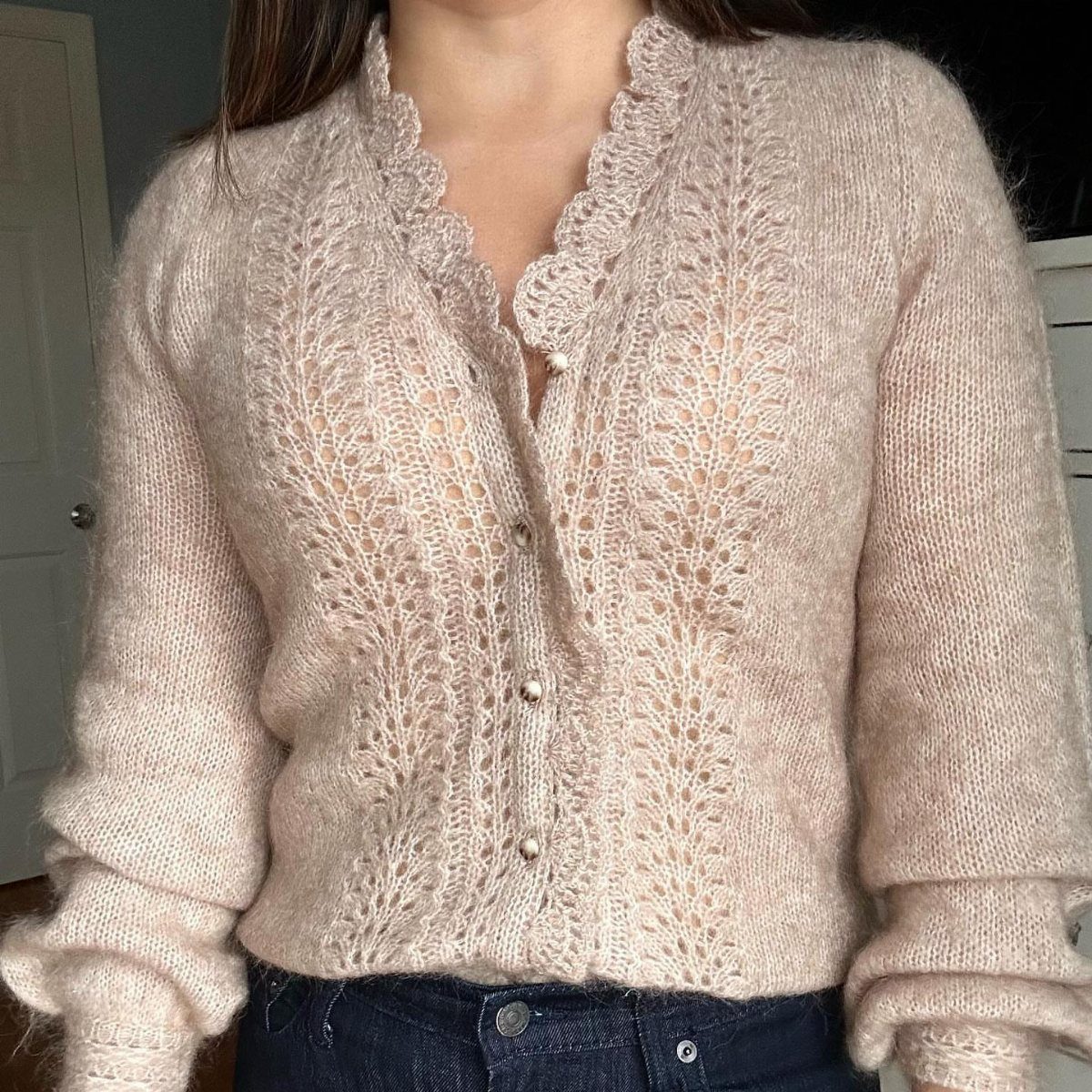 A woman wearing a fuzzy beige lace cardigan tucked into dark blue denim jeans.