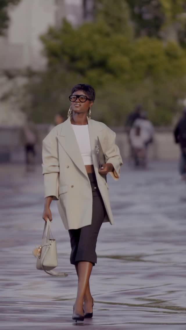 A woman walking in a cream oversized blazer, white top, and black skirt.