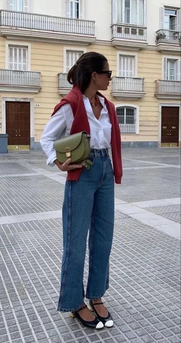 Woman in white shirt and blue jeans with a red sweater draped over her shoulders.