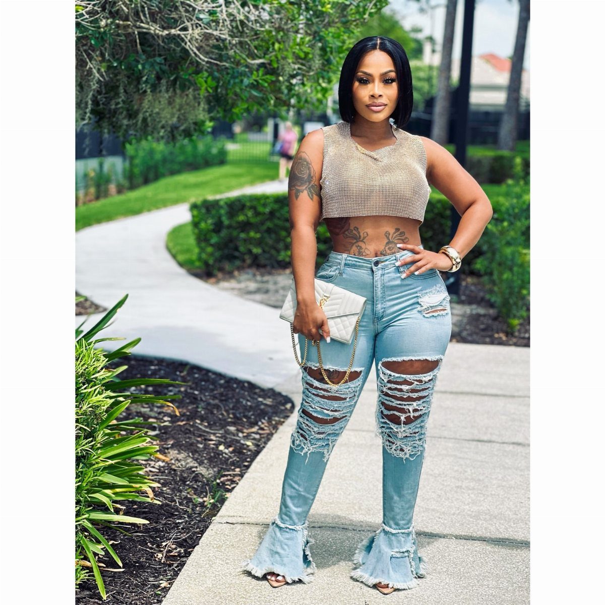 A woman wearing a gold sequined crop top and distressed blue jeans standing on a sidewalk.