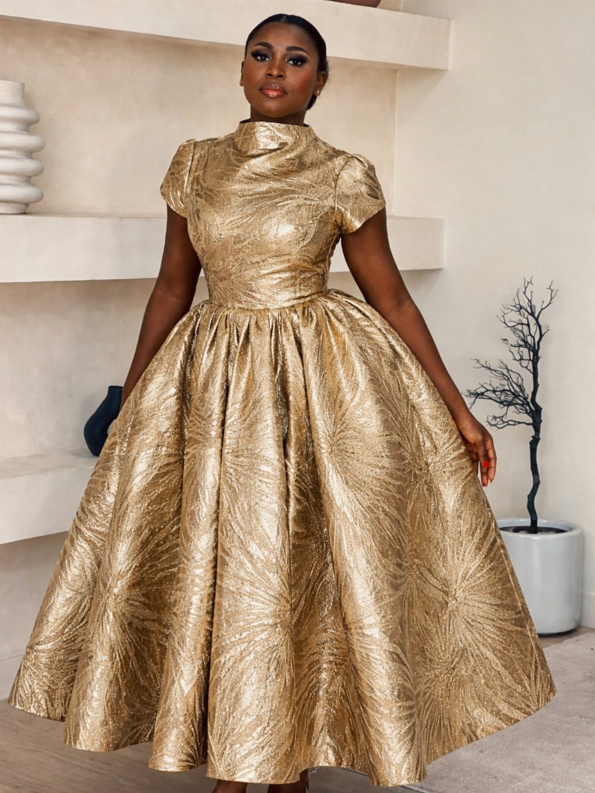 Woman wearing a shimmering gold metallic midi dress with a voluminous pleated skirt.