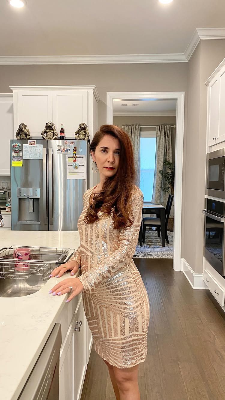 A woman wearing a shimmering gold sequin long-sleeved dress standing in a kitchen.