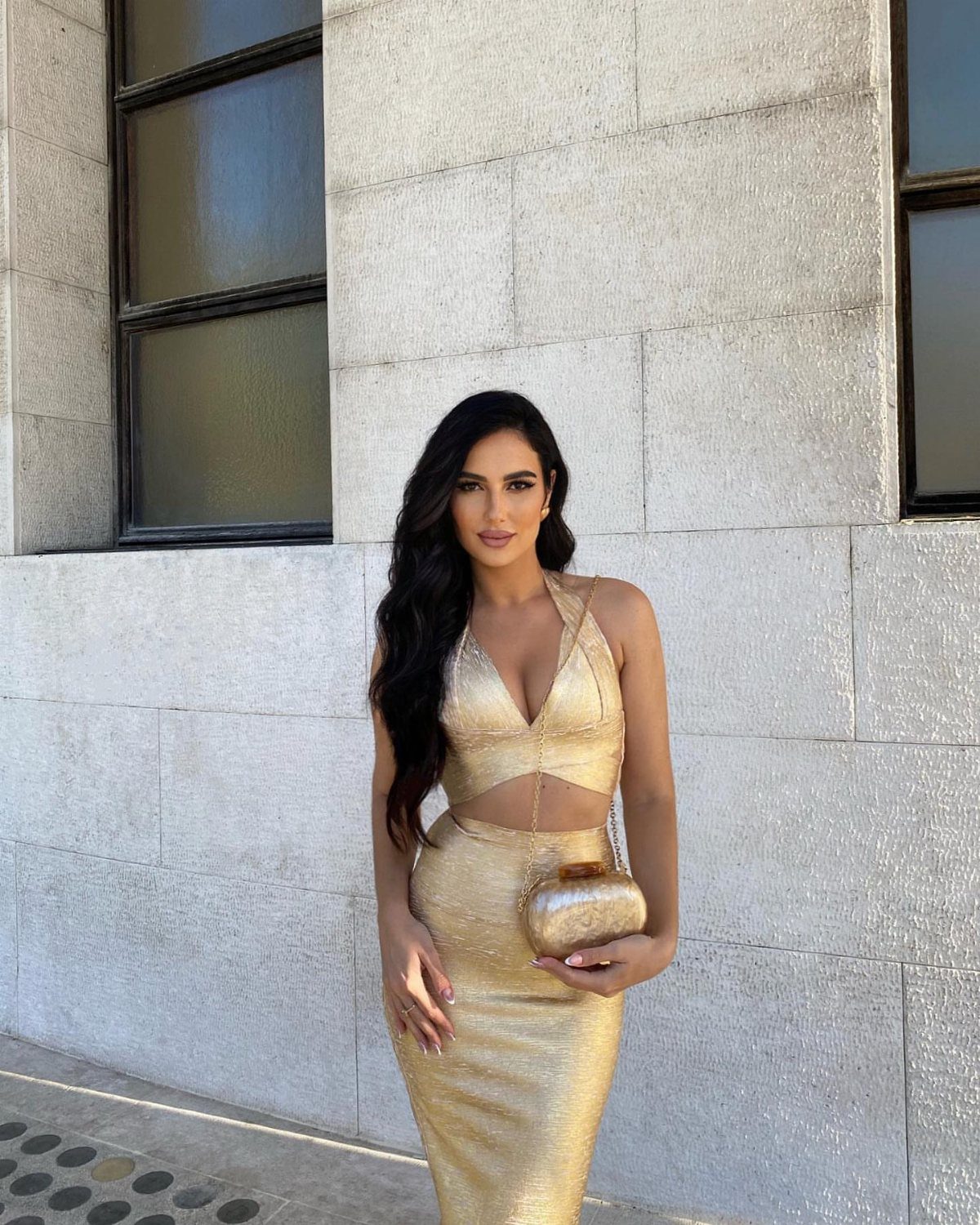 Woman in a shimmering gold two-piece crop top and midi skirt set holding a clutch.