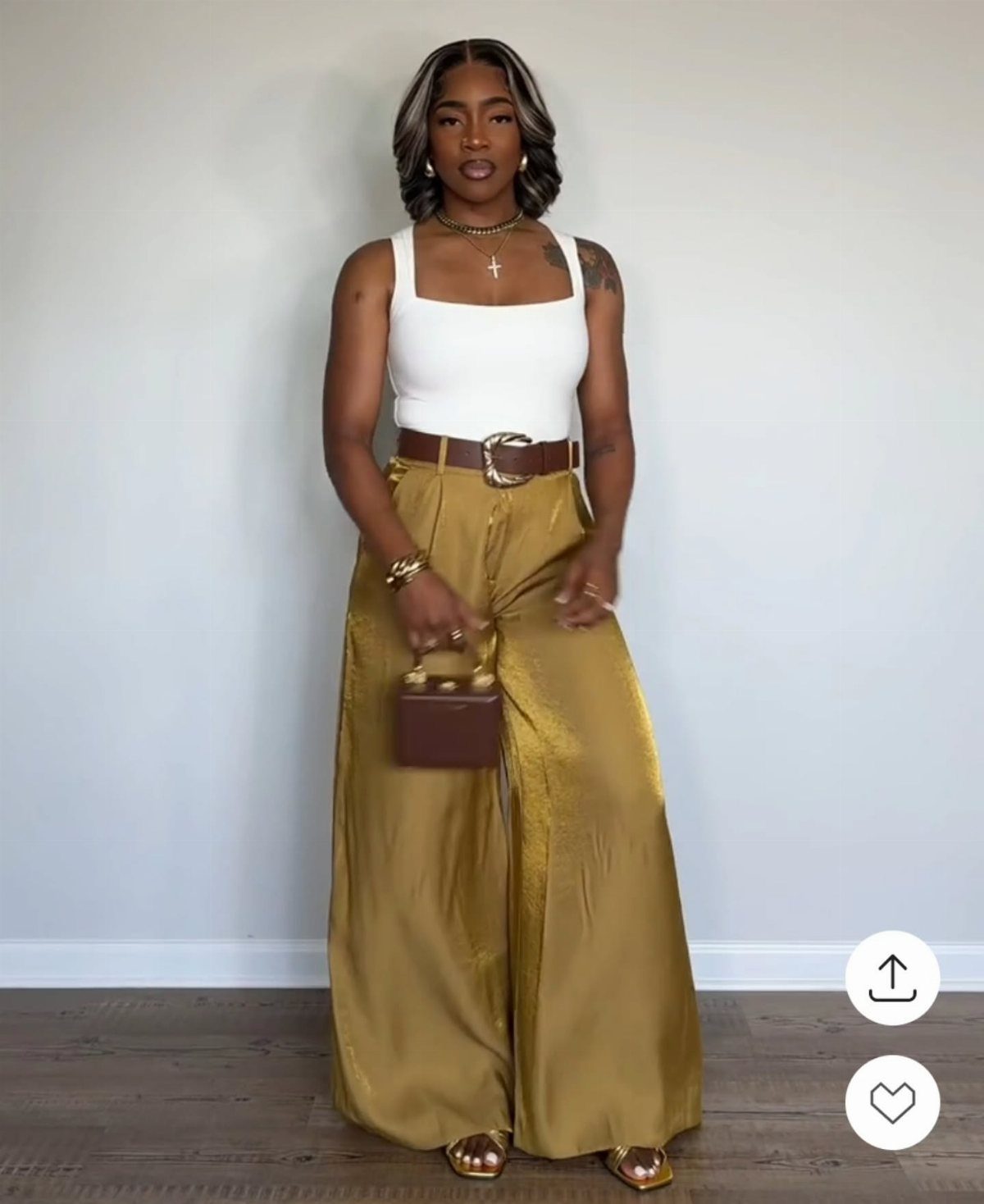 Woman posing in a white tank top and gold wide leg satin pants.