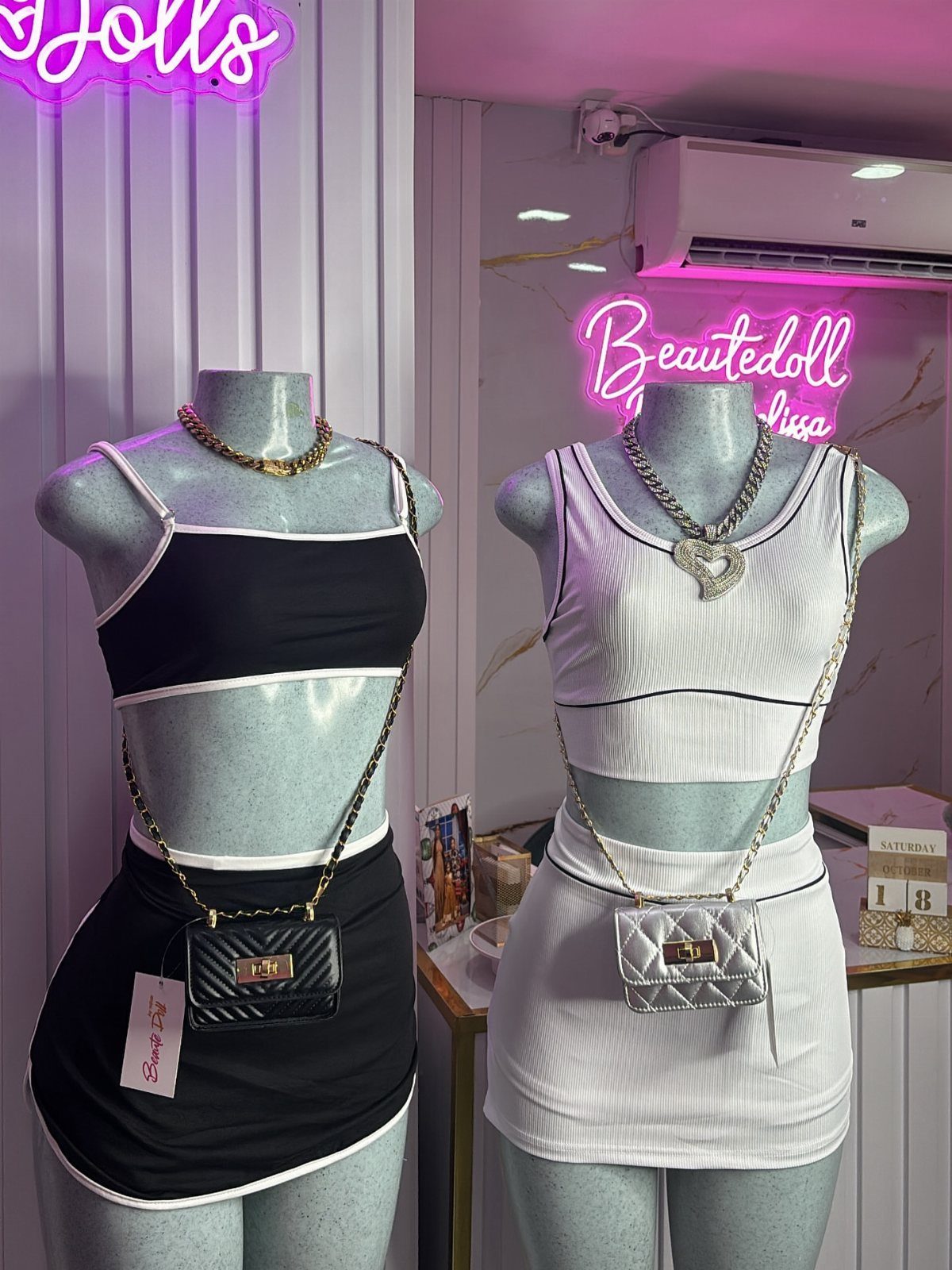 Two mannequins wearing black and white coordinated crop top and mini skirt outfits with small crossbody bags.