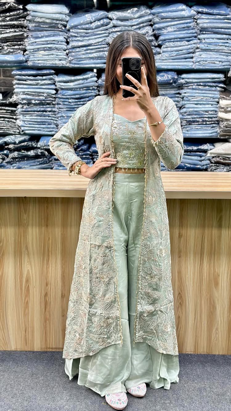 Woman wearing a sage green embroidered long jacket, crop top, and wide-leg trousers.