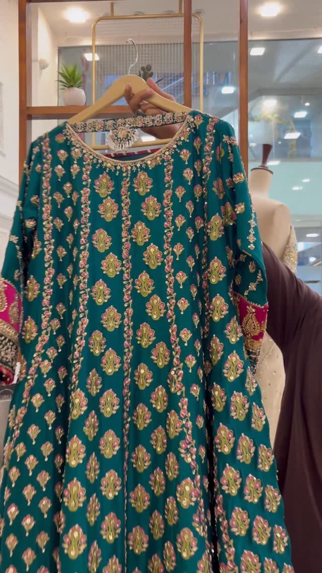 Emerald green silk kurti with gold and pink floral embroidery hanging on a wooden hanger.