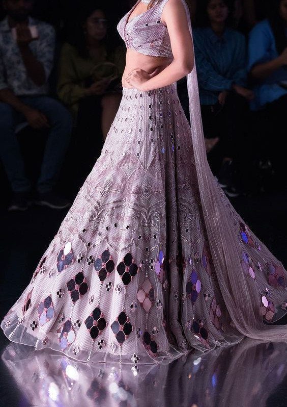 A person wearing a lavender sleeveless crop top and a voluminous embroidered lehenga skirt.