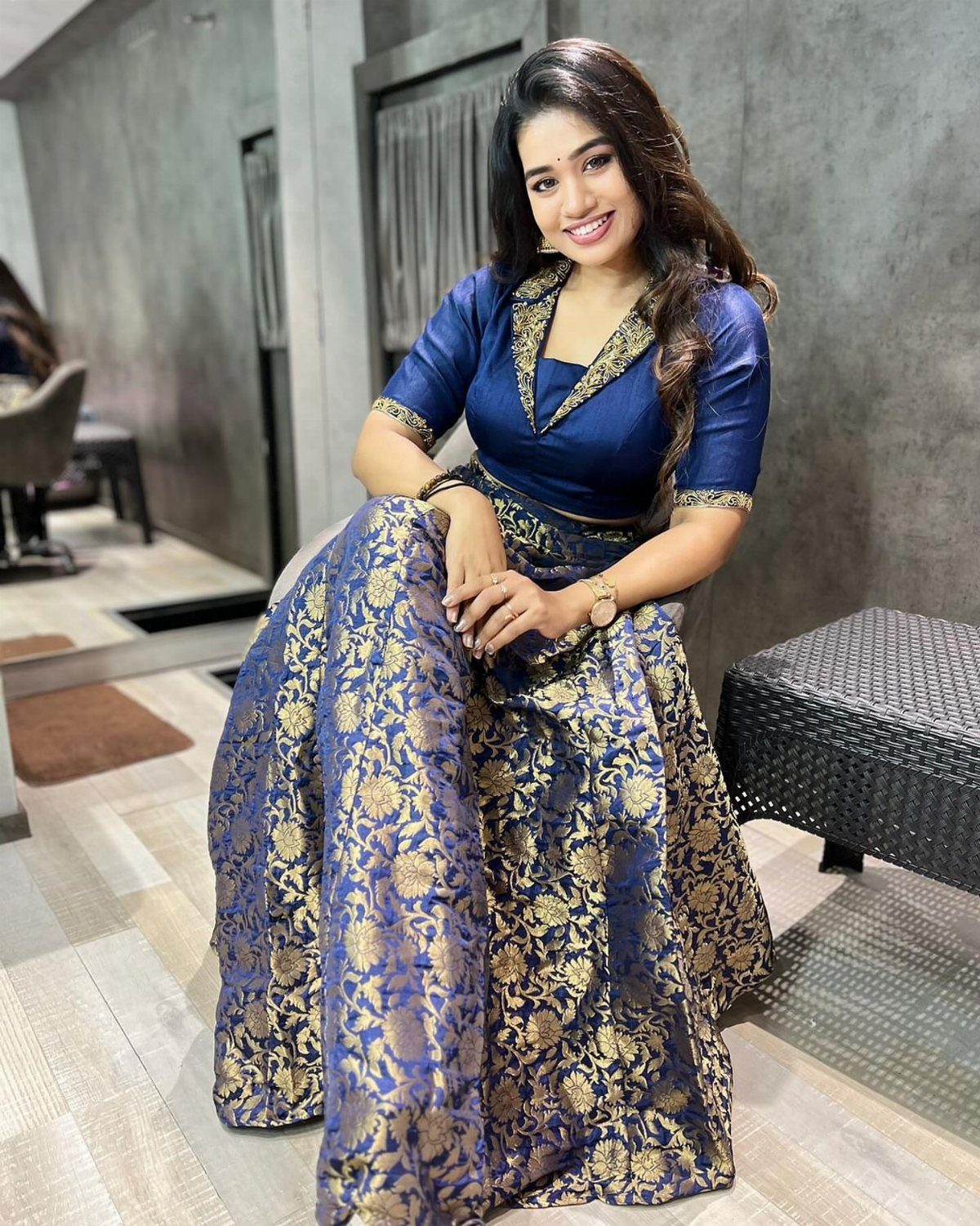A smiling woman wearing a navy blue silk crop top and a gold floral patterned skirt.