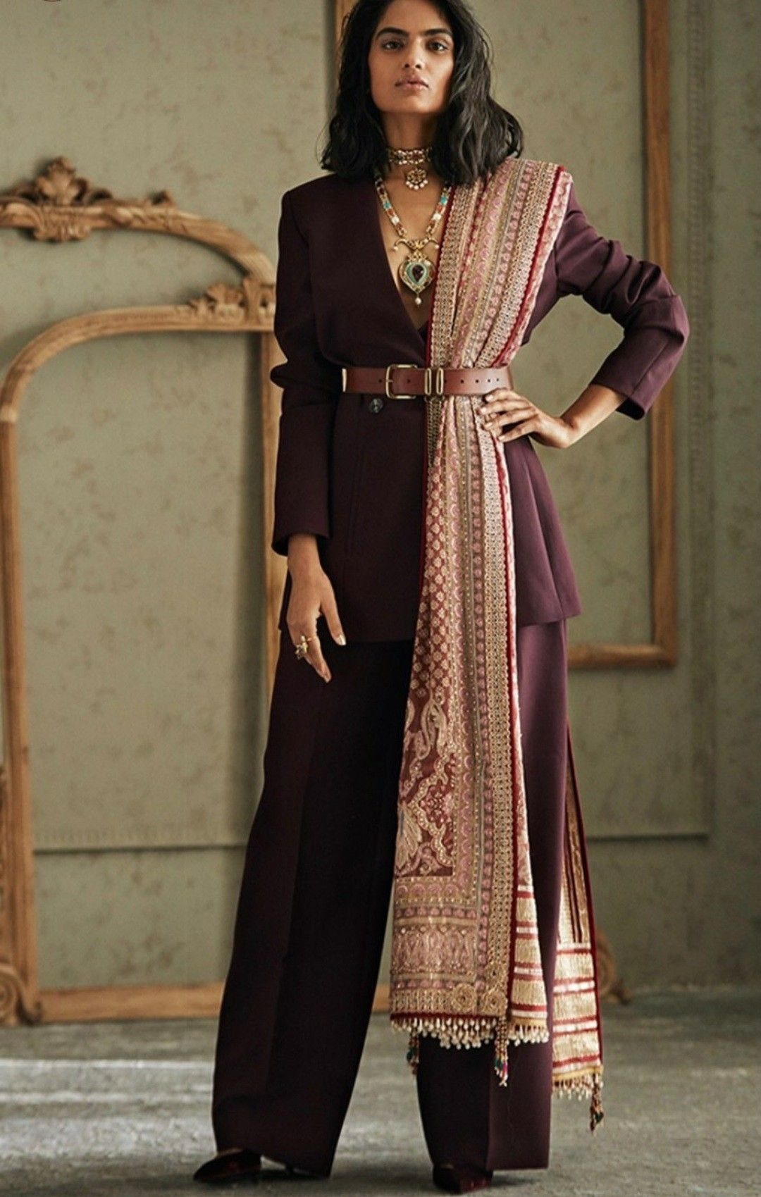 Woman wearing a plum blazer and trousers cinched with a brown leather belt and patterned dupatta.