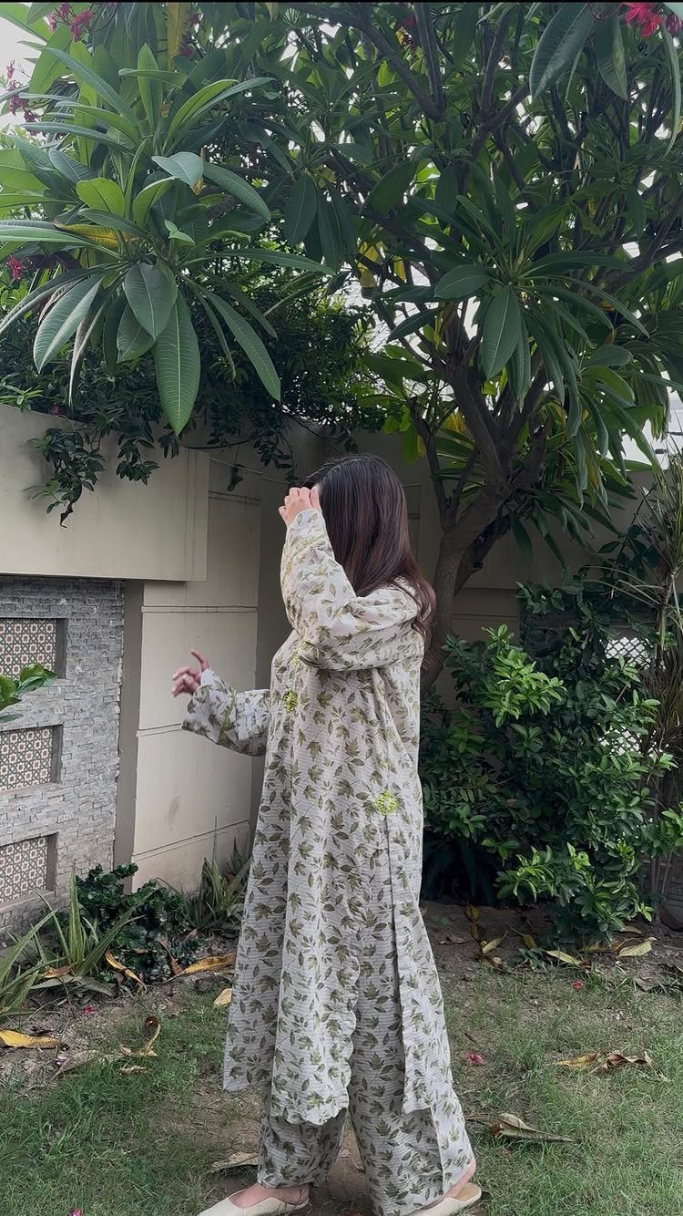 Woman in a floral print tunic and matching wide-leg trousers standing in a lush green garden.