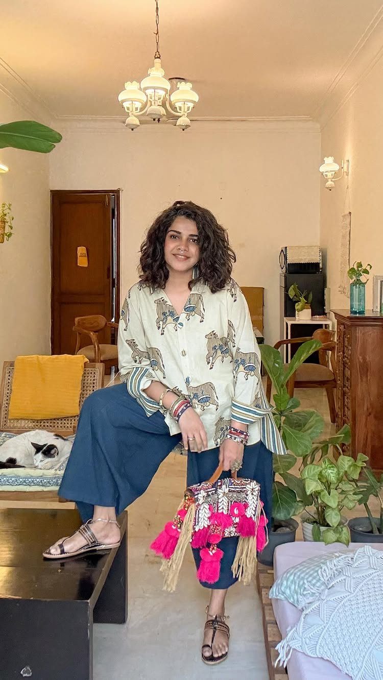 A woman smiling in a printed cotton tunic and dark blue palazzo pants holding a colorful bag.