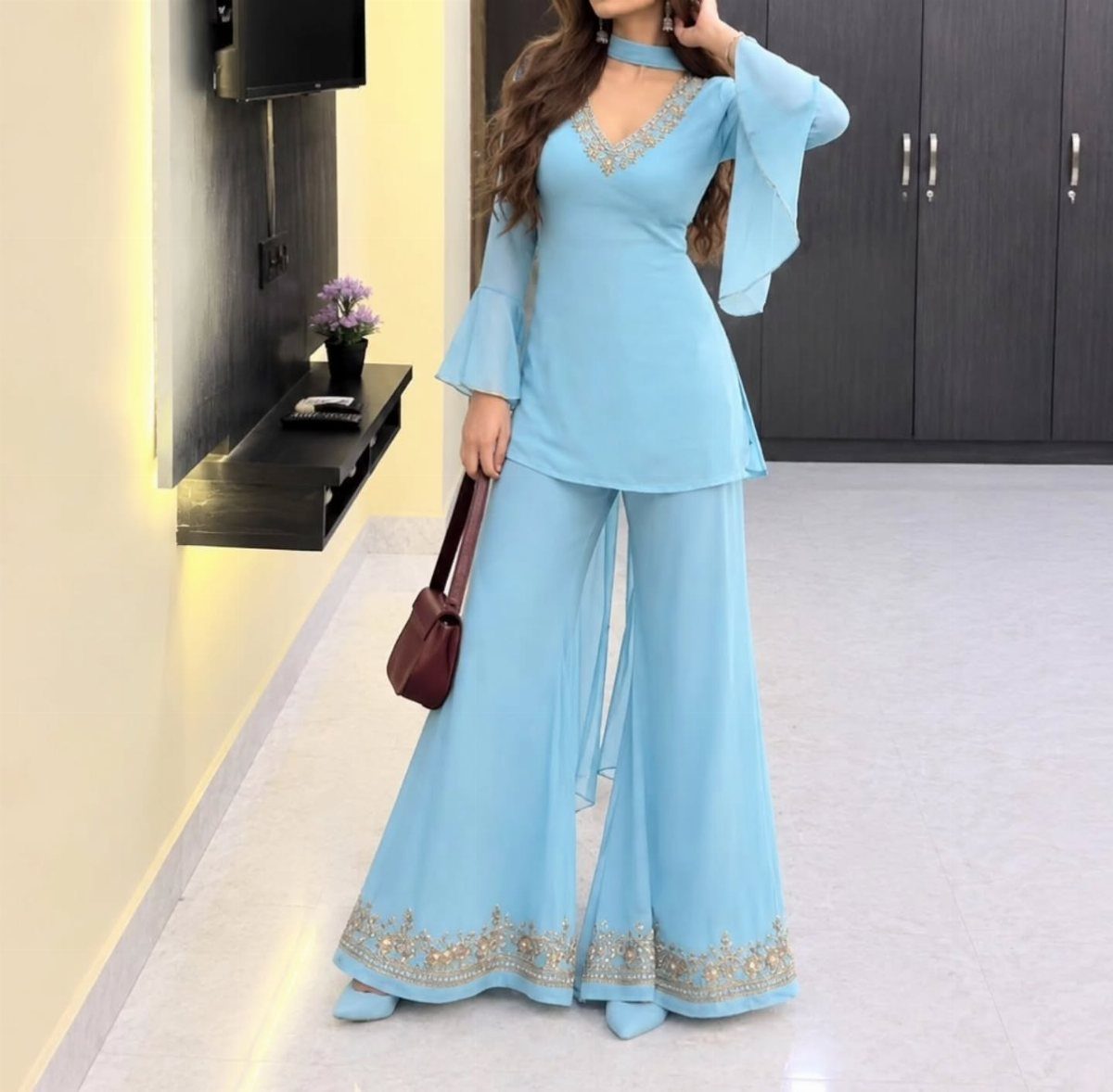 Woman posing in a light blue tunic and flared trousers with gold embroidery.