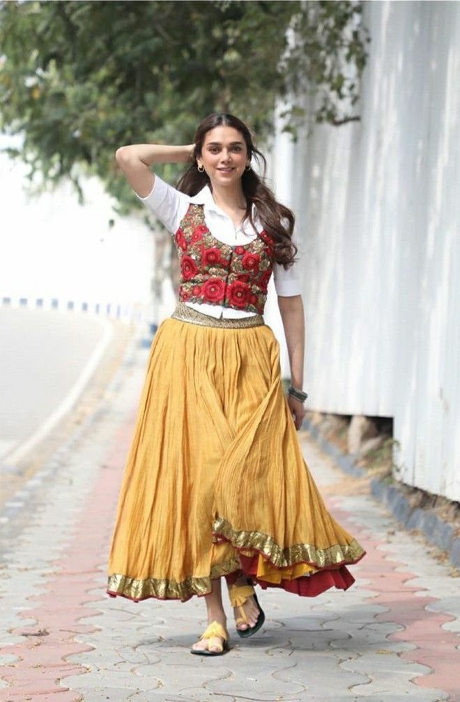 Woman walking in a red embroidered vest and a voluminous yellow layered skirt.