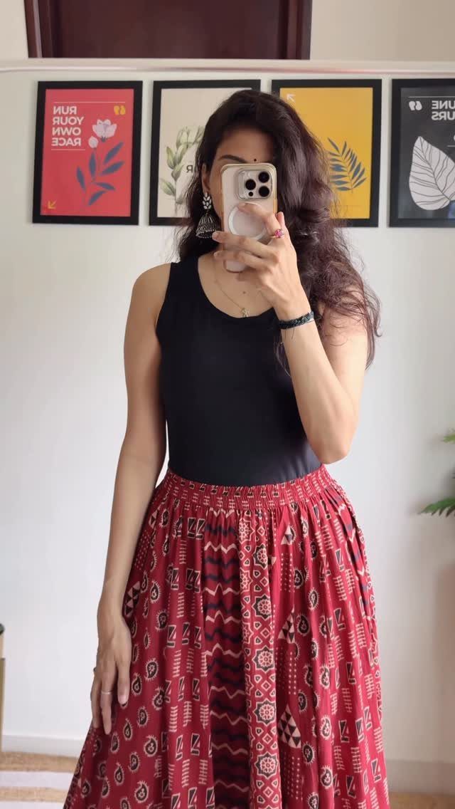 Woman in a black tank top and patterned red maxi skirt taking a mirror selfie.