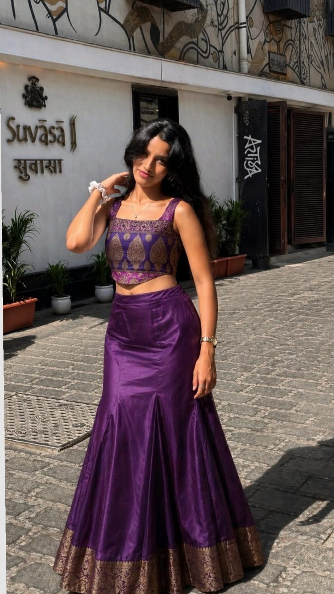 A woman wearing a purple mermaid skirt and a patterned crop top standing on a street.