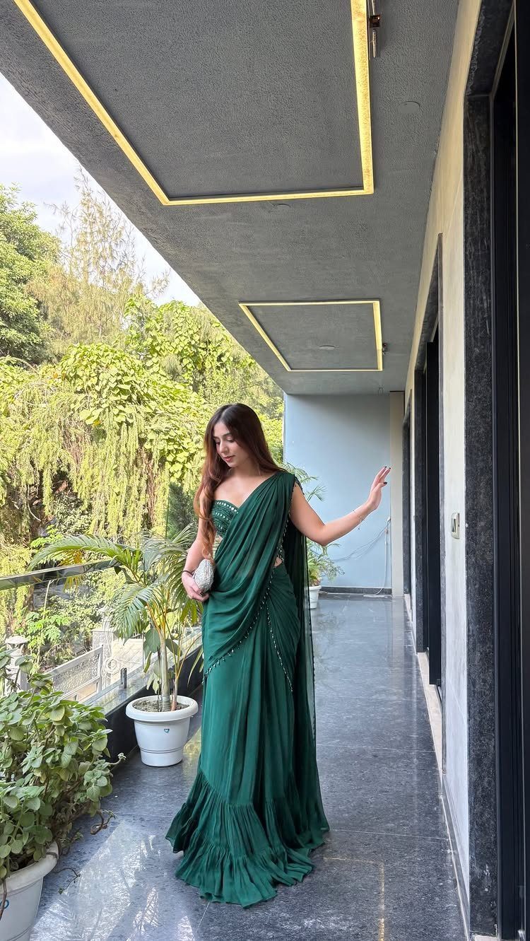 A woman posing on a balcony wearing a modern dark green ruffled saree.