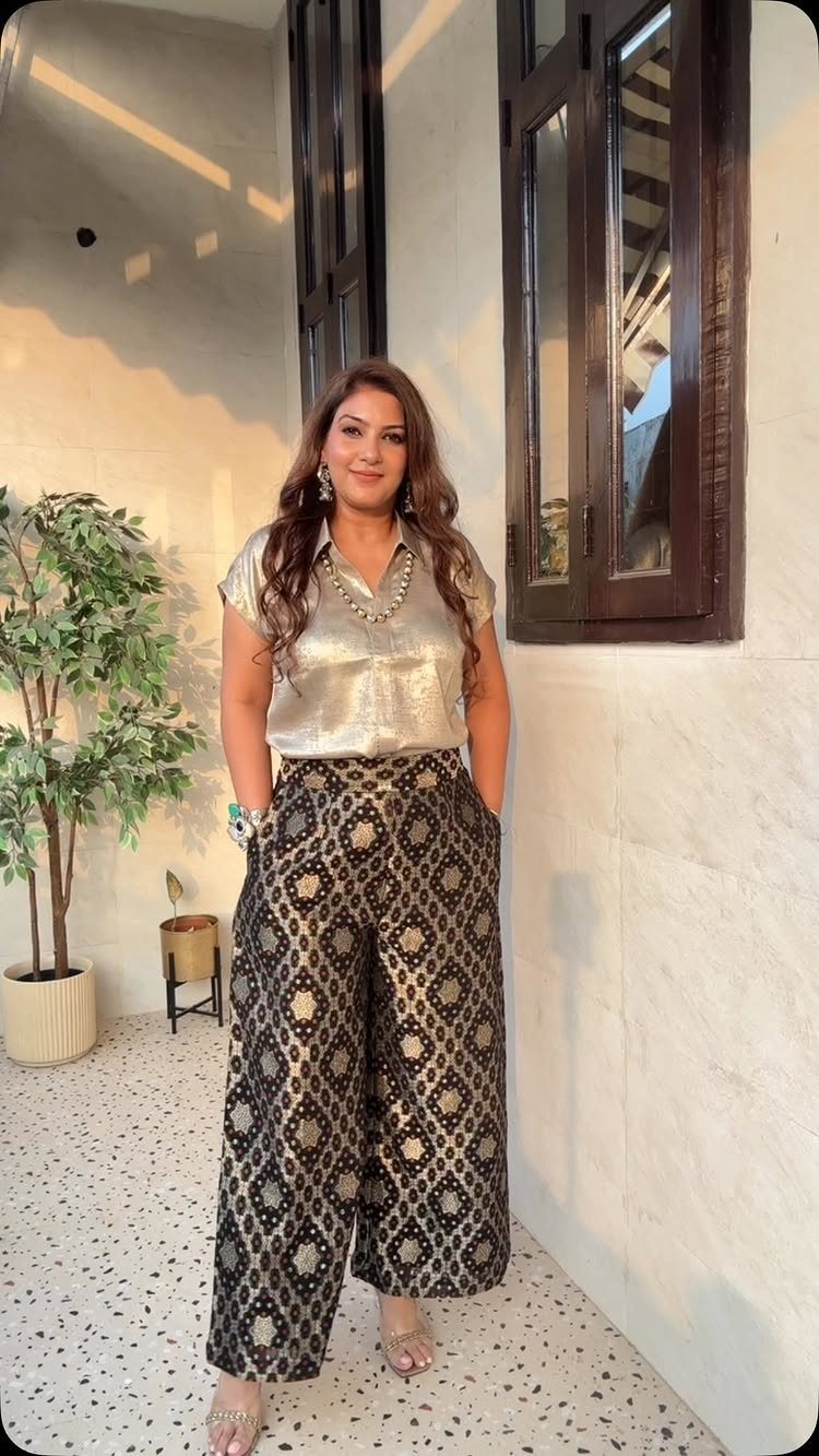 Woman wearing a metallic gold blouse and patterned wide-leg trousers standing outdoors.