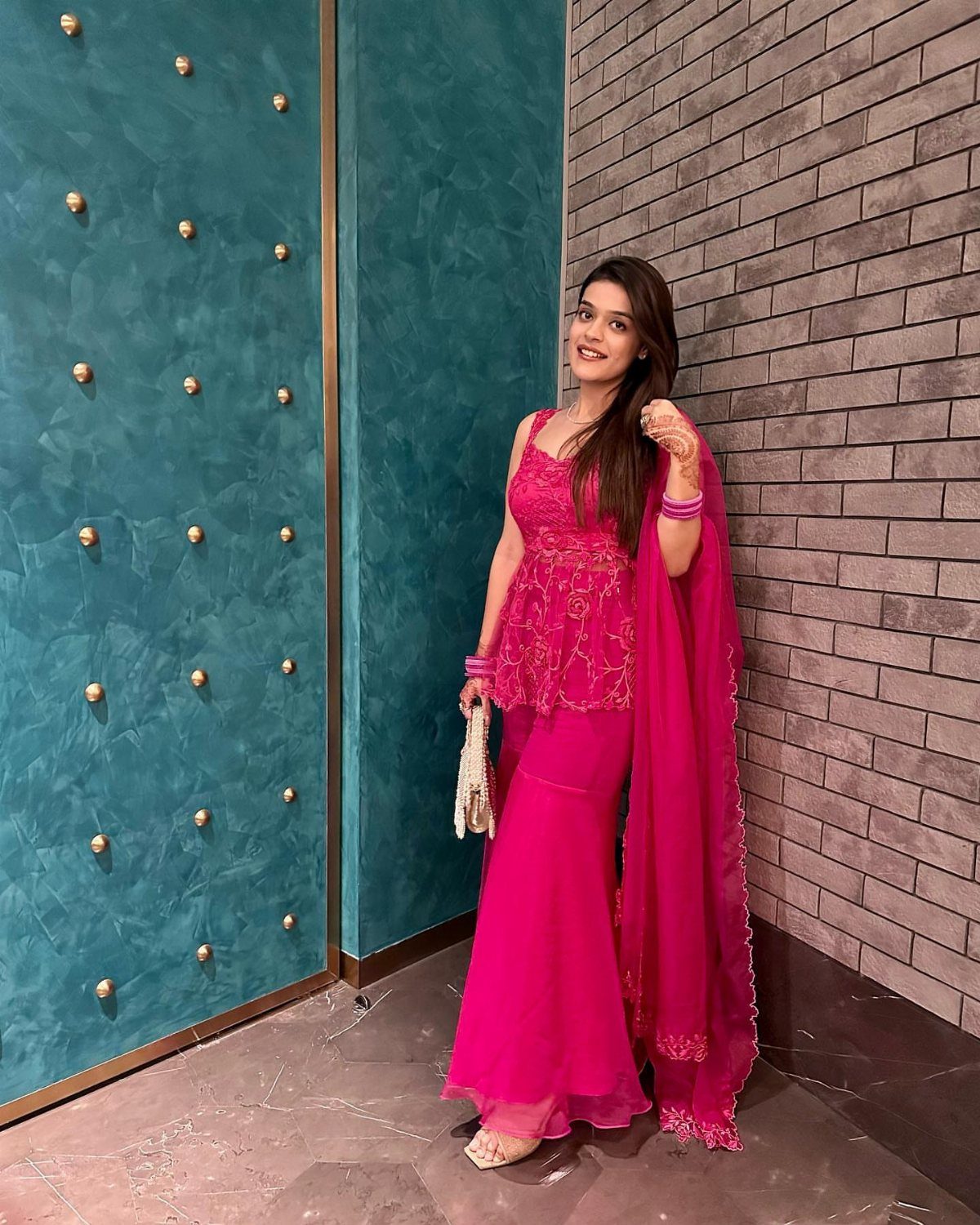 Woman posing in a hot pink gold embroidered spaghetti strap sharara set against textured walls.