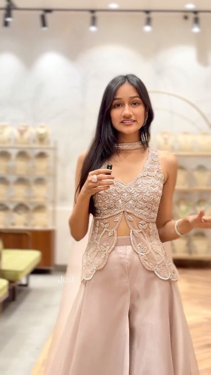 A woman posing in an embellished champagne-colored crop top and wide-leg trousers.