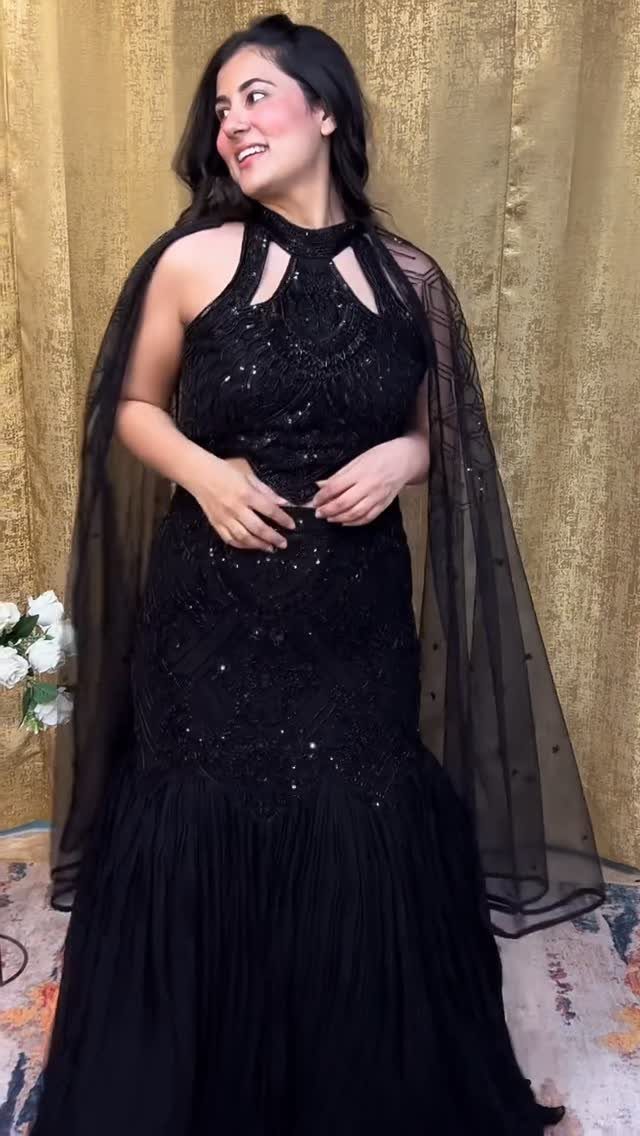 A woman smiling in a black sequined halter gown with a sheer cape against a gold background.