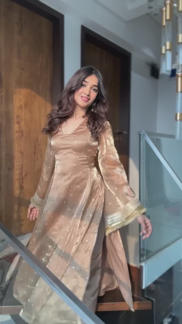 A woman posing in a shimmering champagne-colored Indo-Western suit set with flared sleeves.