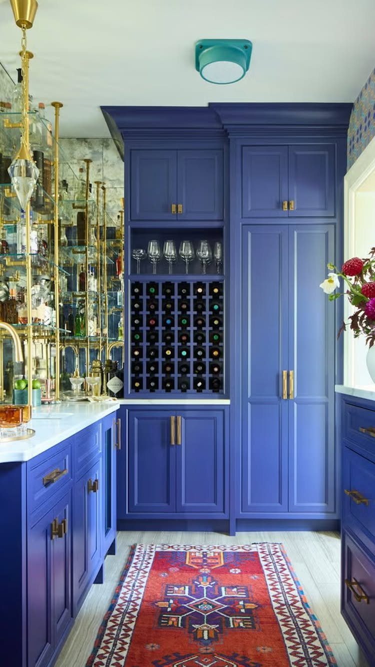 Deep blue kitchen cabinets with gold hardware and a patterned red rug on the floor.