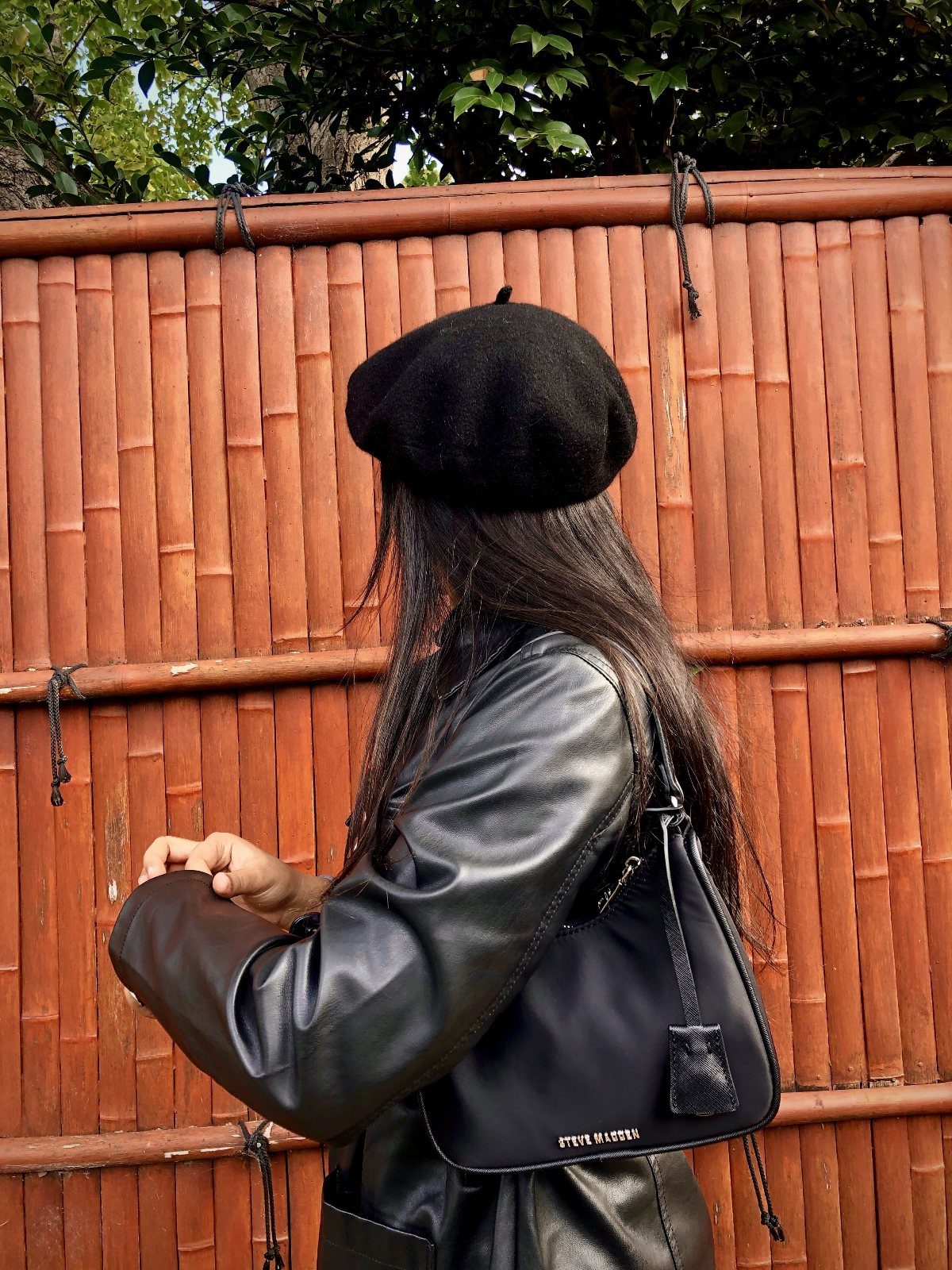 A person wearing a black beret and leather jacket with a small black handbag.