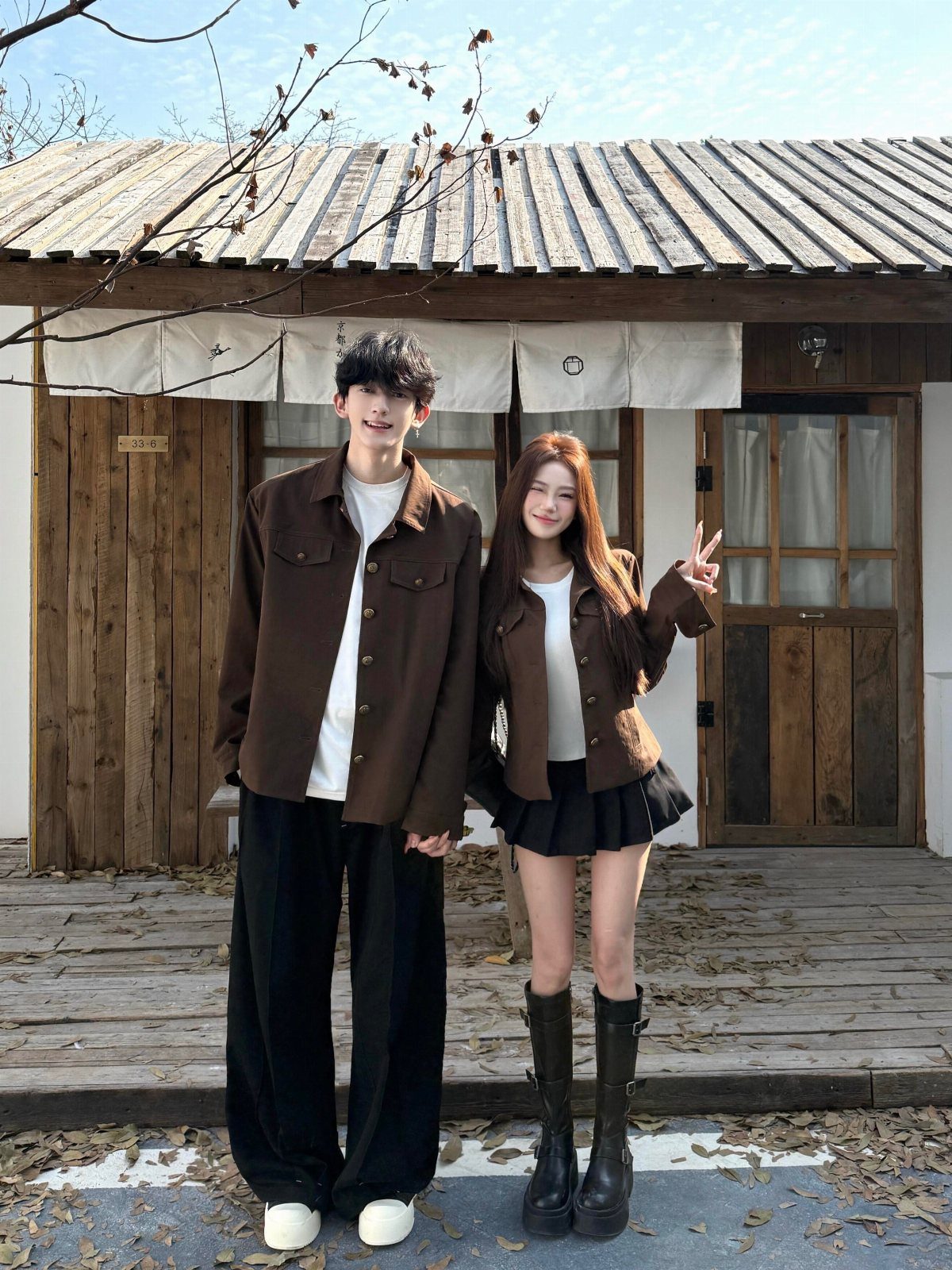 A young couple posing in matching brown jackets and coordinated street style outfits outdoors.