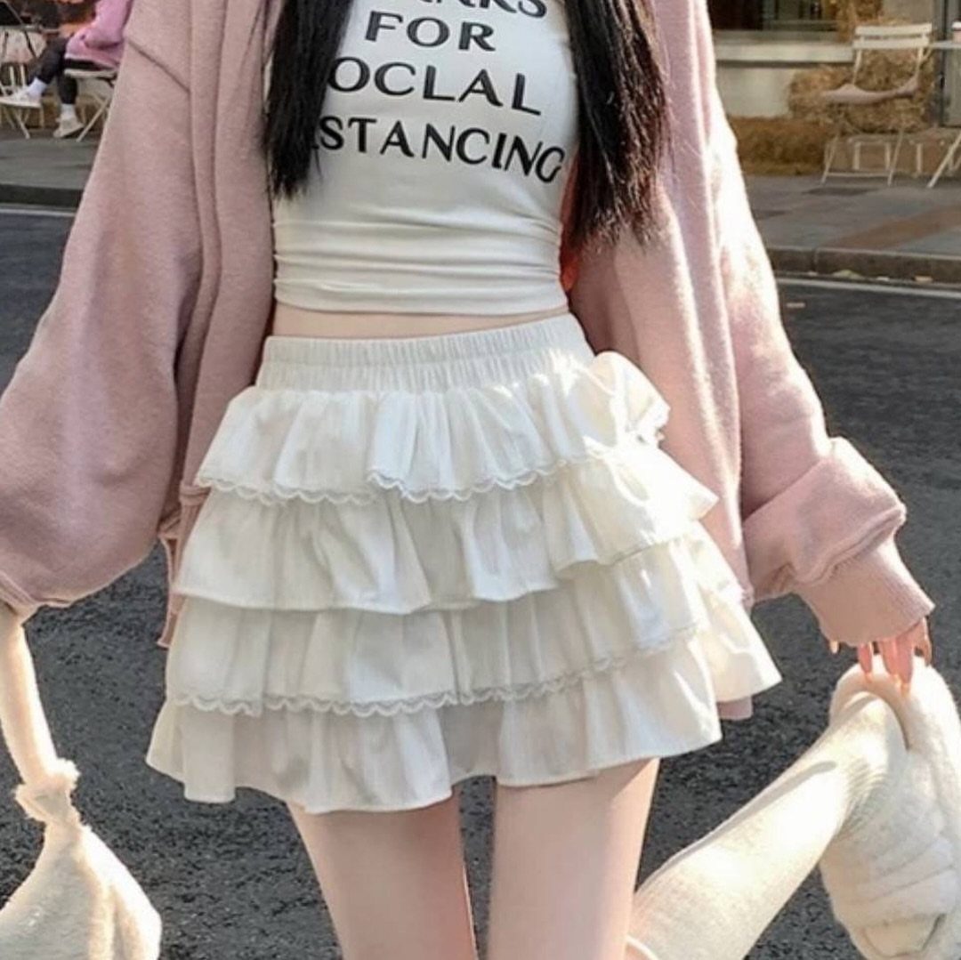 A person wearing a white tiered ruffled mini skirt and a pink oversized cardigan outdoors.