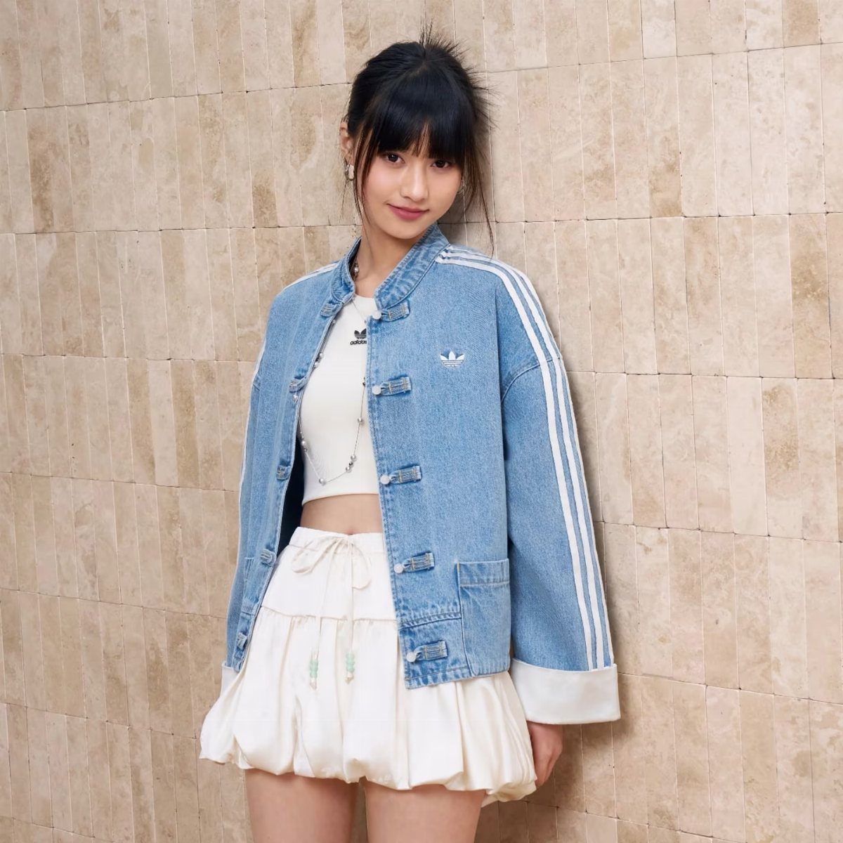 A young woman wearing an oversized denim jacket and a white ruffled skirt.
