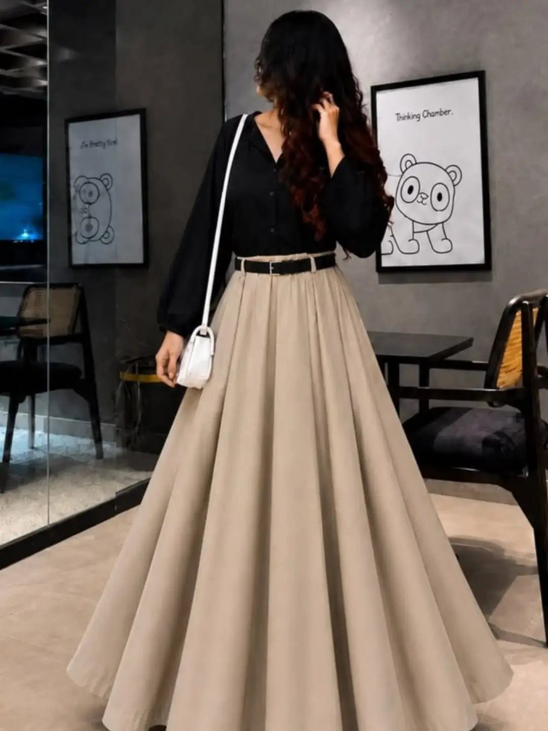 Woman wearing a black long-sleeved blouse and a flowing beige pleated maxi skirt.