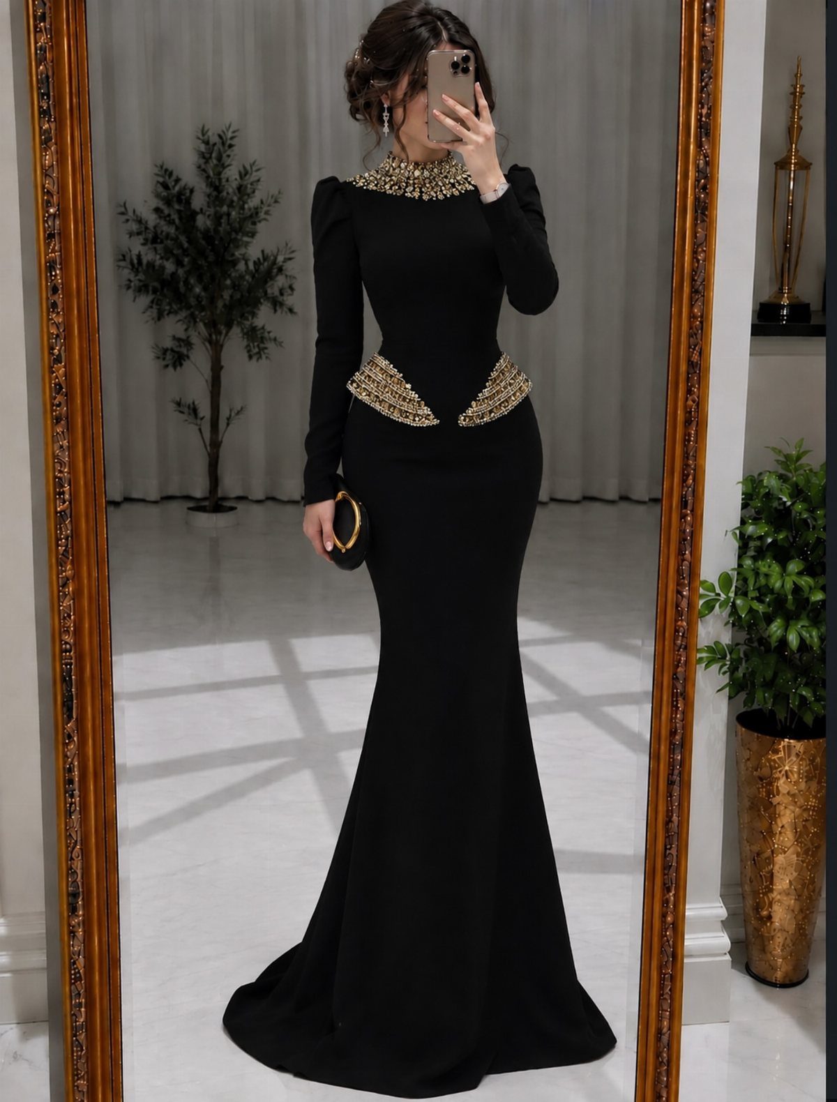 Woman wearing a black mermaid gown with gold beaded details posing for a mirror selfie.